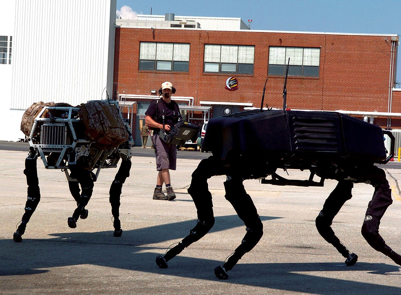 BigDog, un robot quadrupède à actionnement hydraulique, marchant près d'un MV-22 Osprey